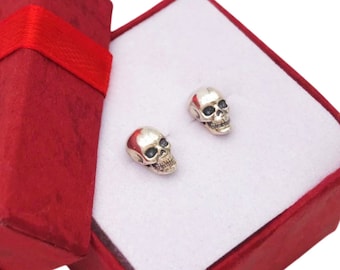 Könnte beinhalten: Ein Paar silberne Totenkopf-Ohrstecker in einer roten Geschenkbox mit roter Schleife.