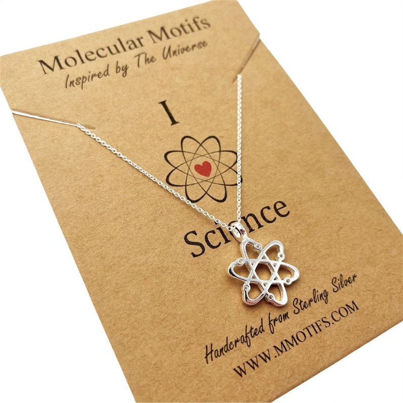 May include: A silver necklace with an atom pendant and the words "I love Science" on a brown card. The card also says "Molecular Motifs Inspired by The Universe" and "Handcrafted from Sterling Silver" with the website address "www.mmotifs.com".