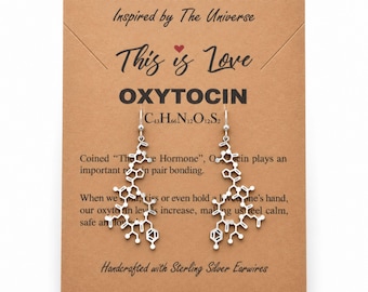 May include: Silver-toned earrings shaped like the oxytocin molecular structure, displayed on a brown card labeled Molecular Motifs, This is Love, OXYTOCIN, C43H66N12O12S2, and text describing the hormone, with sterling silver earwires.
