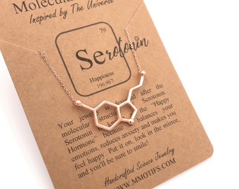 May include: A gold necklace with a pendant shaped like the molecular structure of serotonin. The necklace comes with a card that reads "Serotonin, Happiness 196.967. Your jewelry is designed after the molecular structure of Serotonin, the "Happy Hormone" because serotonin reduces anxiety and makes you feel happy. Put it on, look in the mirror, and you'll be sure to smile!" Handcrafted Science Jewelry WWW.MMOTIFS.COM
