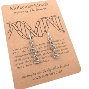Peut inclure: Boucles d'oreilles en argent en forme de double hélice d'ADN. Les boucles d'oreilles sont sur une carte avec le texte "Molecular Motifs Inspired by The Universe" et "Handcrafted with Sterling Silver Earwires WWW.MMOTIFS.COM".