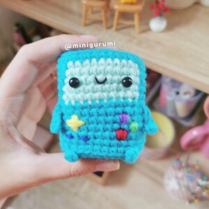 May include: A crocheted blue character with a happy face, yellow, red, purple and green details. The character is holding a star in its hand. @minigurumi