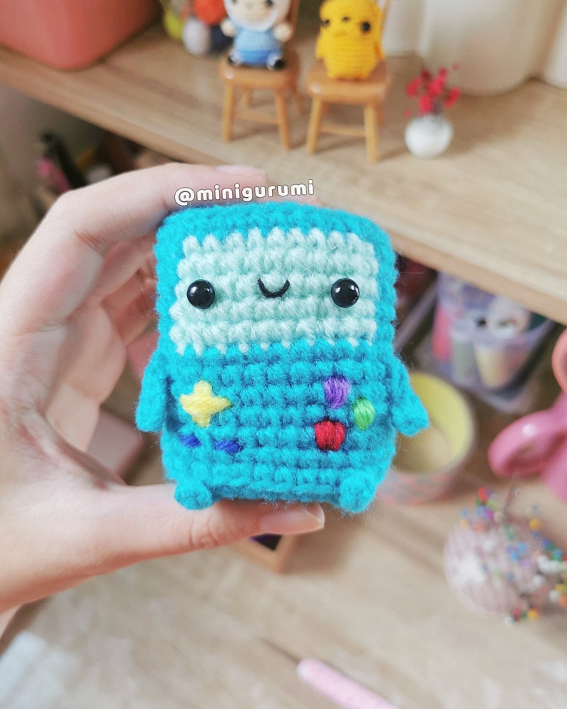May include: A crocheted blue character with a happy face, yellow, red, purple and green details. The character is holding a star in its hand. @minigurumi