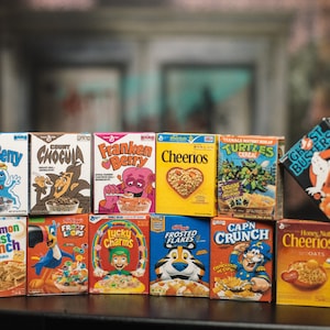 May include: A collection of 10 colorful cereal boxes featuring various cartoon characters and mascots. The boxes include Boo-Berry, Count Chocula, Franken Berry, Cheerios, Teenage Mutant Ninja Turtles Cereal, Froot Loops, Lucky Charms, Frosted Flakes, Cap'n Crunch, and Cinnamon Toast Crunch.