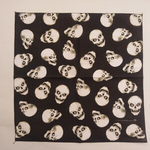 May include: A square bandana featuring a repeating pattern of off-white human skulls on a solid black background. The skulls are oriented in various directions across the fabric, displaying detailed eye sockets, nasal cavities, and teeth.