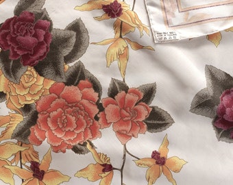 May include: A white silk scarf with a floral pattern featuring red, orange, and yellow flowers with green and brown leaves. The scarf has a tag that reads "Thai Silk 100% Made in Thailand."