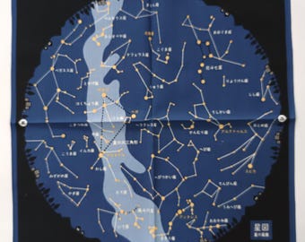 May include: Square, navy blue handkerchief featuring a celestial map design. The map depicts constellations in gold against a dark blue background, with Japanese text and a black border. The handkerchief is folded.