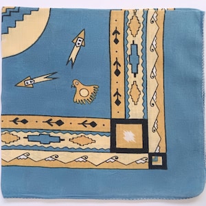 May include: Square blue and yellow patterned scarf. The scarf features geometric and stylized bird and arrow designs. The border has a repeating pattern of diamonds and rectangles. The scarf is made of a soft, lightweight fabric.