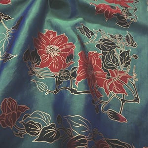 May include: Close-up of a teal fabric with a floral pattern. Large red flowers with white outlines and black leaves are scattered across the fabric. The fabric has a slight sheen, creating a sense of depth and texture.