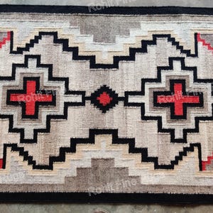 May include: Rectangular rug with a geometric pattern in neutral tones. The design features black, red, and tan shapes, including crosses and stepped elements. The rug has a black border and a textured appearance.