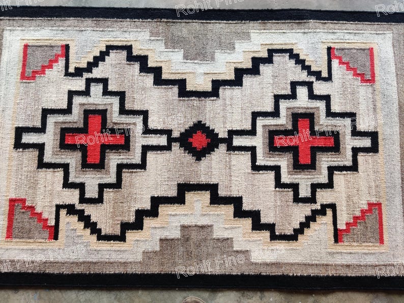 May include: Rectangular rug with a geometric pattern in neutral tones. The design features black, red, and tan shapes, including crosses and stepped elements. The rug has a black border and a textured appearance.