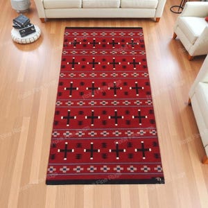 Könnte beinhalten: Ein rechteckiger roter Teppich mit einem geometrischen Muster aus schwarzen Kreuzen und weißen Akzenten. Der Teppich hat einen Rand und liegt auf einem Parkettboden. Der Teppich ist ein dekorativer Bodenbelag.