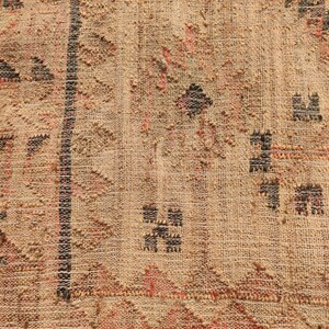 Puede incluir: Primer plano de un textil tejido con un fondo beige texturizado. El dise&ntilde;o presenta formas geom&eacute;tricas en negro, rojo y marr&oacute;n, incluyendo tri&aacute;ngulos y patrones de diamantes. Una franja negra vertical recorre el centro.