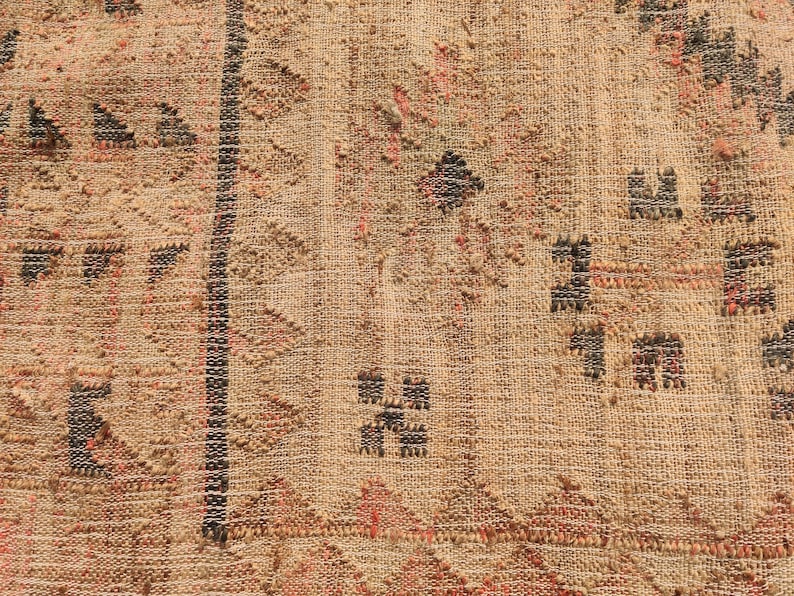 Puede incluir: Primer plano de un textil tejido con un fondo beige texturizado. El dise&ntilde;o presenta formas geom&eacute;tricas en negro, rojo y marr&oacute;n, incluyendo tri&aacute;ngulos y patrones de diamantes. Una franja negra vertical recorre el centro.