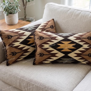 May include: Two rectangular throw pillows featuring a geometric pattern in shades of brown, tan, cream, and black. The design includes repeating arrow motifs and jagged, stepped diamond shapes across the front surface of each pillow cover.