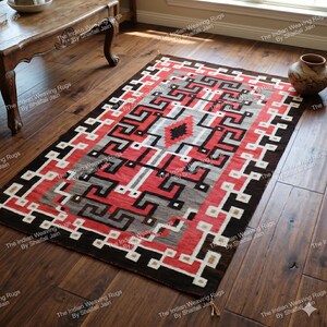 Op de afbeelding: Een rechthoekig vloerkleed met een geometrisch patroon in rood, zwart, wit en grijs. Het vloerkleed heeft een donkerbruine rand en een centraal ontwerp met ruit- en zigzagvormen. Het vloerkleed ligt op een houten vloer.