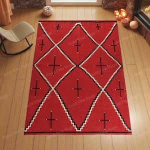 Op de afbeelding: Een rood vloerkleed met een geometrisch patroon. Het vloerkleed heeft een herhalend ruitontwerp met zwart-witte zigzagranden en zwarte kruisvormen. Het vloerkleed is gemaakt van geweven materiaal en wordt op een houten vloer getoond.