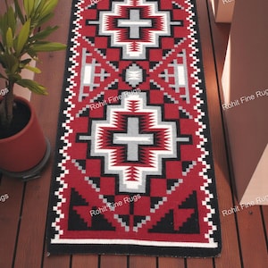 Op de afbeelding: Een rechthoekig rood tapijt met een geometrisch patroon in zwart, wit en grijs. Het tapijt heeft een zwarte rand en de tekst "Rohit Fine Rugs" staat erop gedrukt. Het tapijt ligt op een houten oppervlak.