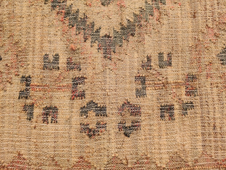 Puede incluir: Primer plano de un textil tejido con fondo beige y patrones geom&eacute;tricos en negro, rojo y marr&oacute;n. La textura parece &aacute;spera y natural, con nudos visibles y variaciones en el tejido.