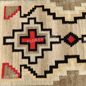 May include: Close-up of a woven rug with a geometric pattern. The design features black, beige, and red shapes, including crosses and zigzags. The rug has a textured appearance and a border of black and beige stripes.