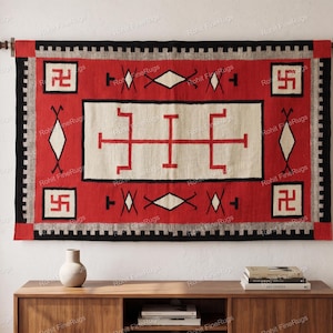 Op de afbeelding: Een rechthoekig geweven wandkleed met een centraal crèmekleurig paneel met rode geometrische lijnpatronen, omringd door een brede rode rand met zwarte en witte accenten, inclusief vier hoekvierkanten met rode swastika-symbolen.
