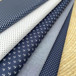 Könnte beinhalten: Auswahl an Stoffen mit marineblauen und weißen Mustern. Designs umfassen weiße Sterne, Punkte und Anker. Ein unifarbener grauer Stoff ist ebenfalls sichtbar. Die Stoffe sind in einer geschichteten Anordnung angeordnet, die die Mustervielfalt zeigt.