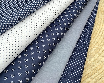 Op de afbeelding: Assortiment van marineblauwe en witte stoffen met patronen. Ontwerpen omvatten witte sterren, stippen en ankers. Er is ook een effen grijze stof zichtbaar. De stoffen zijn in een gelaagde opstelling gerangschikt, die de verscheidenheid aan patronen laat zien.