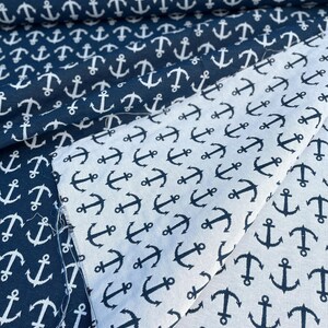 Può includere: Tessuto nautico blu navy e bianco con un motivo ripetuto di ancore. Il tessuto è piegato, mostrando sia uno sfondo blu navy con ancore bianche che uno sfondo bianco con ancore blu navy. Ideale per progetti di cucito.