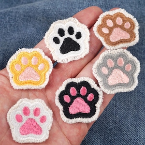 May include: Six embroidered paw print patches in various colours, including yellow, brown, grey, black, and white. The paw prints have pink accents.