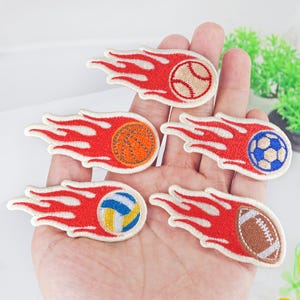 May include: Five embroidered iron-on patches featuring different sports balls on fire. The balls include a baseball, basketball, volleyball, soccer ball, and football.