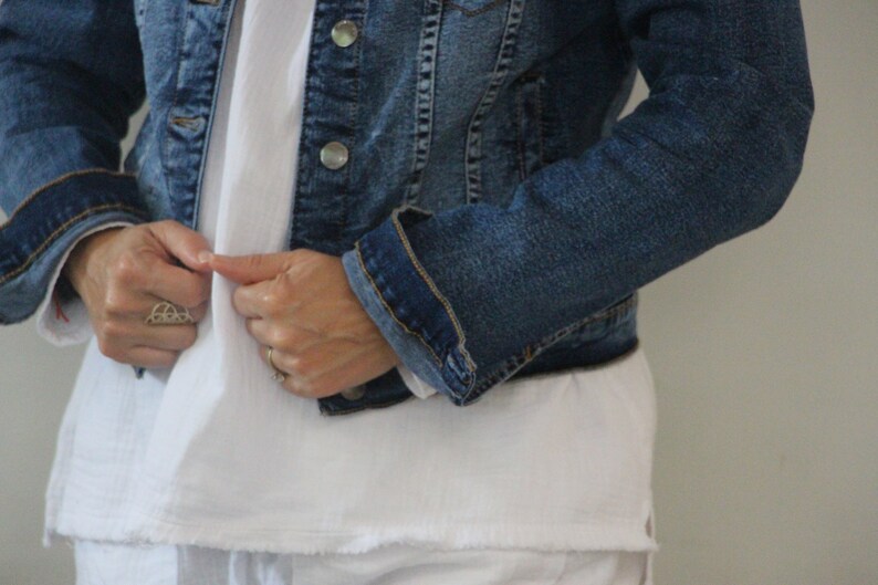Puede incluir: Una persona lleva una chaqueta vaquera azul sobre una camiseta blanca. La chaqueta est&aacute; desabrochada y la persona est&aacute; ajustando el cuello.