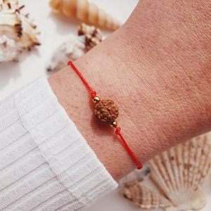 May include: A red string bracelet with a brown wooden bead and gold accents.
