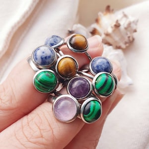 May include: A set of nine rings with different colored gemstones. The rings are made of silver and have a simple design. The gemstones are blue, green, purple, and brown.