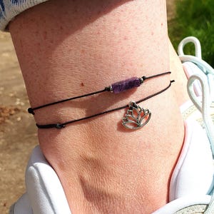 May include: A black ankle bracelet with a purple stone and a silver lotus charm.