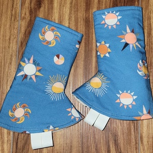 May include: Two blue oven mitts with a white background and a pattern of suns and stars in shades of yellow, orange, and brown.