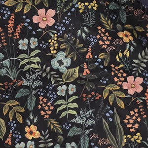 May include: A black fabric featuring a dense botanical print of various wildflowers and foliage. The pattern includes pink, yellow, orange, and light blue flowers interspersed with green leaves and stems, creating a detailed floral design.