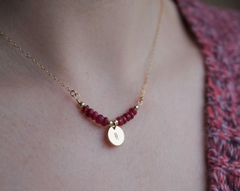 May include: A gold chain necklace with a small gold disc pendant and a row of red gemstone beads.