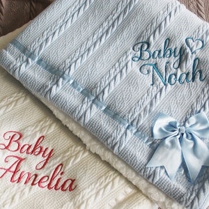 May include: Two knitted baby blankets, one white with red embroidery that says "Baby Amelia" and one light blue with blue embroidery that says "Baby Noah" and a light blue satin bow.