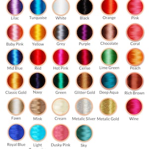 Op de afbeelding: Een kleurenkaart met 25 verschillende garenkleuren, waaronder lila, turquoise, wit, zwart, oranje, roze, babyroze, geel, grijs, paars, chocolade, koraal, middeblauw, rood, roze, kersenrood, limoengroen, perzik, klassiek goud, marineblauw, groen, glittergoud, diepblauw, donkerbruin, lichtbruin, mink, cr&egrave;me, metallic zilver, metallic goud, wijnrood, koningsblauw, licht turquoise, poederroze en hemelsblauw. De kaart is gelabeld met "Thread Colour Chart" en "Options Sheet: 1".