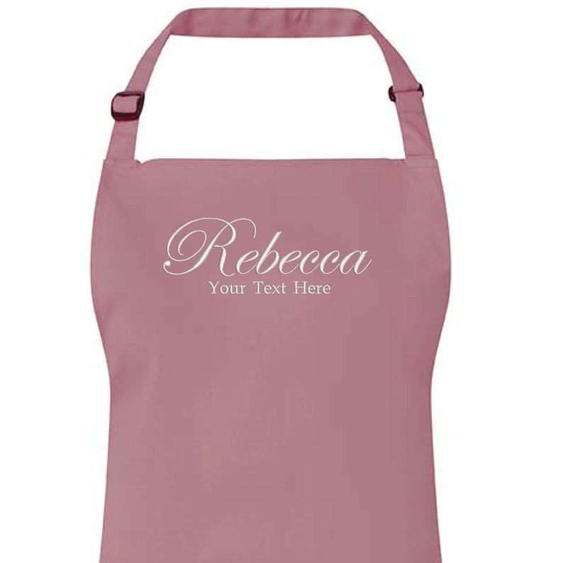 Op de afbeelding: Een roze schort met de naam "Rebecca" en de tekst "Your Text Here" in wit cursief schrift.