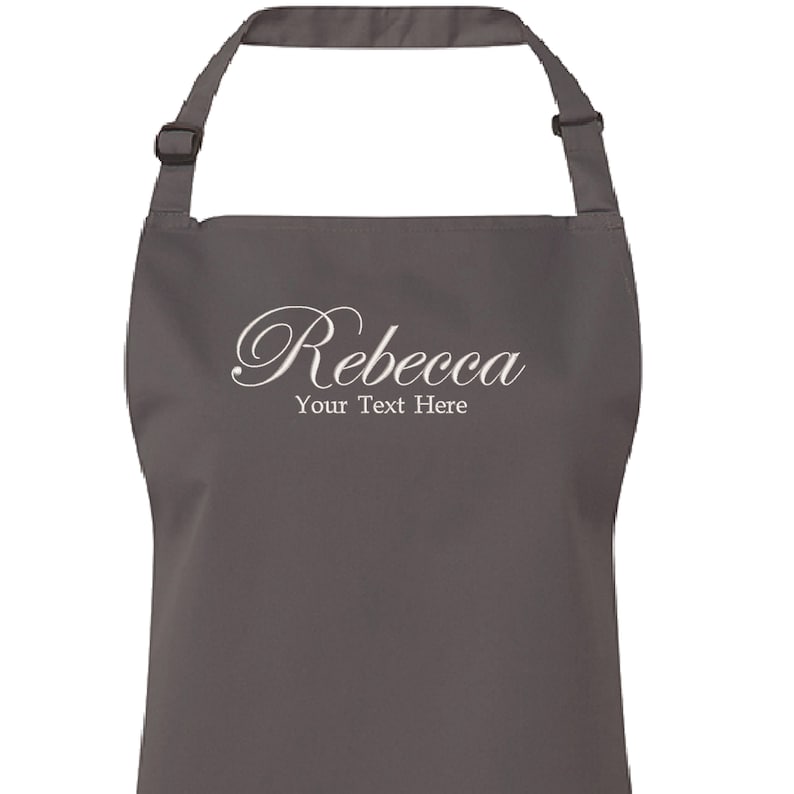 Op de afbeelding: Een grijze schort met de naam "Rebecca" en de tekst "Your Text Here" geborduurd in wit.