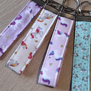 May include: Four colorful keychains with unicorn designs. The keychains are made of fabric and have silver key rings. The designs include a purple and white unicorn, a pink and white unicorn, a white and pink unicorn, and a blue and white unicorn.