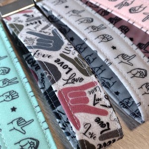May include: Four keychains with different patterns. The keychains are made of fabric and feature a variety of hand signs and the word "love" in different fonts. The keychains are all attached to silver key rings.