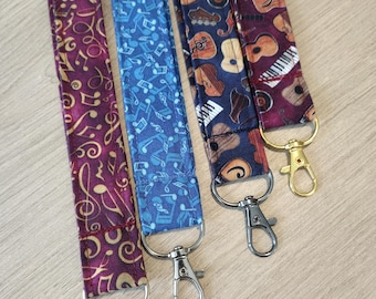 May include: Four fabric lanyards with metal swivel clasps. The lanyards feature musical instrument and music note patterns in various colors, including purple, blue, and navy. The clasps are silver and gold.