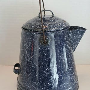May include: A vintage blue enamelware coffee pot with white speckles. The pot has a lid, a spout, and a handle with a wooden grip. The pot is a classic camping or kitchen item.