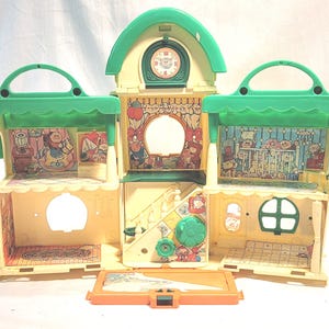 May include: A vintage, multi-sectioned dollhouse toy in shades of green and yellow. The dollhouse features a clock, various rooms with printed interior scenes, and a handle for carrying. The toy is open, revealing the interior details.
