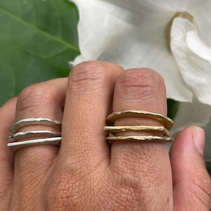 Può includere: Due anelli impilati, uno d'argento e uno d'oro, con una texture martellata. Gli anelli sono indossati su un dito.