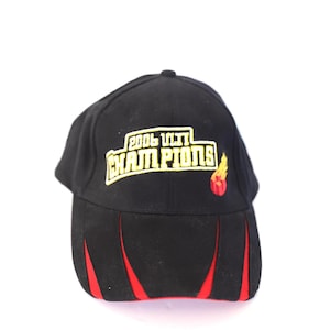 May include: Black baseball cap with red accents and the text "2006 CITY CHAMPIONS" in yellow. The cap features a flame graphic. The hat is a sports-themed accessory.