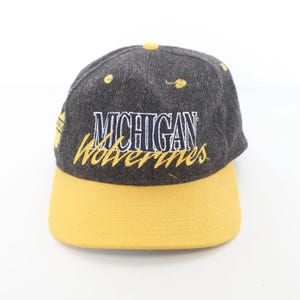 May include: A gray and yellow baseball cap with the text "Michigan Wolverines" embroidered on the front.