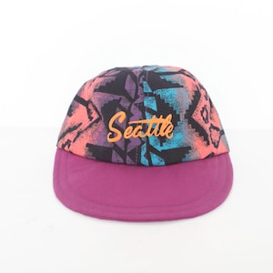 May include: A purple and black baseball cap with a colourful geometric pattern and the word "Seattle" in orange lettering.